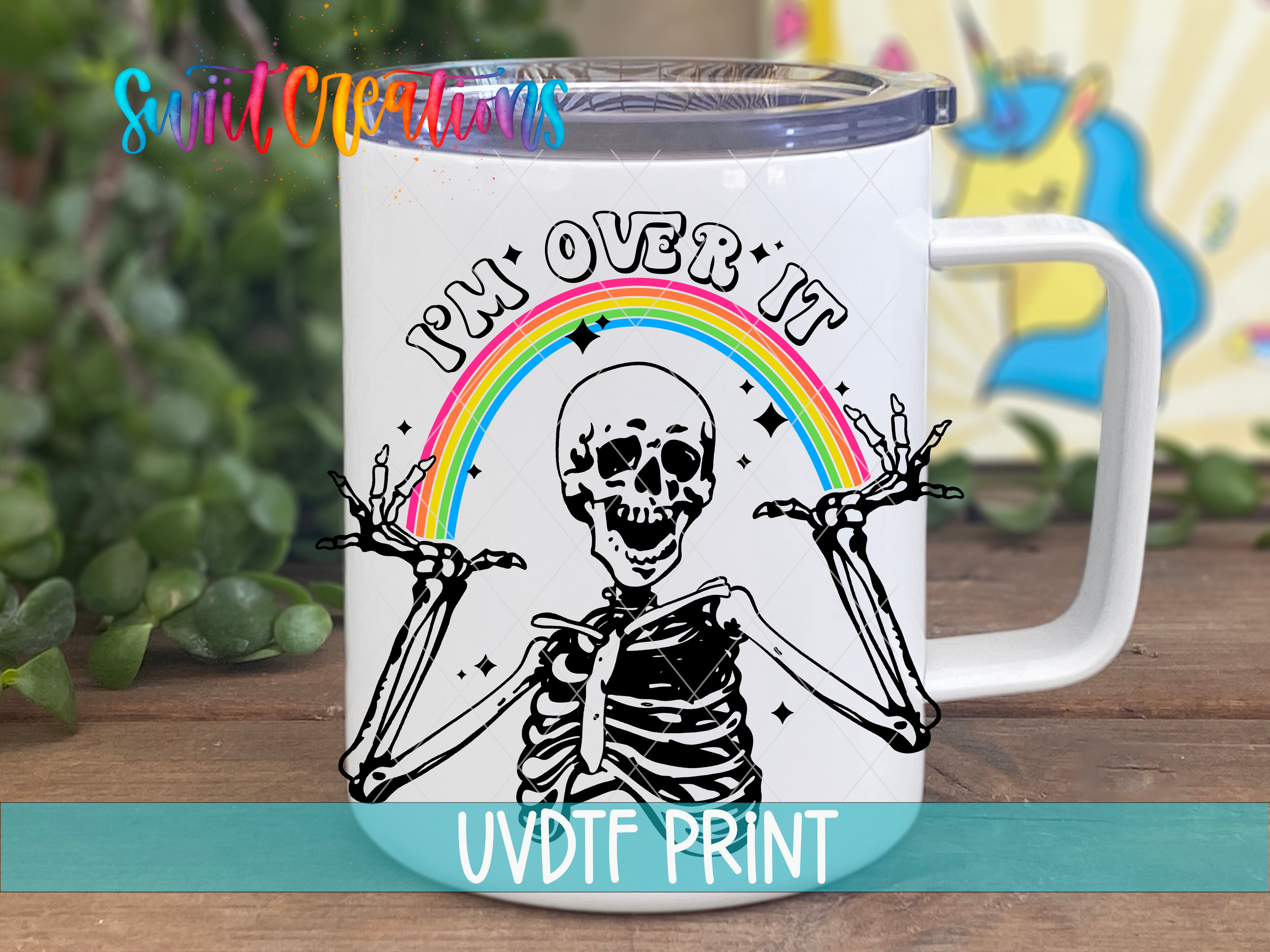 A white mug with a skeleton graphic and a rainbow graphic, along with the text "I'm over it" and "PM over it" printed on it.