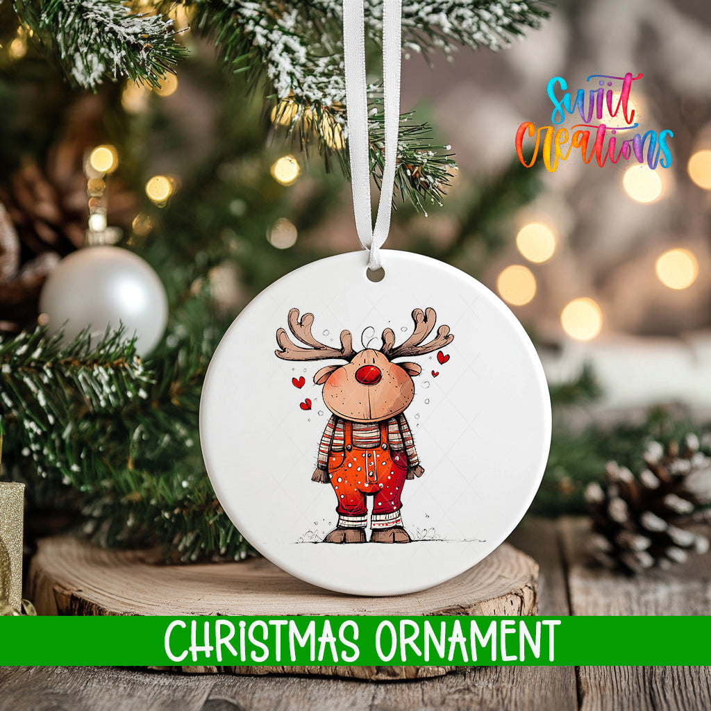 A white Christmas ornament featuring a cartoon reindeer with antlers and a red nose, hanging on a tree branch.