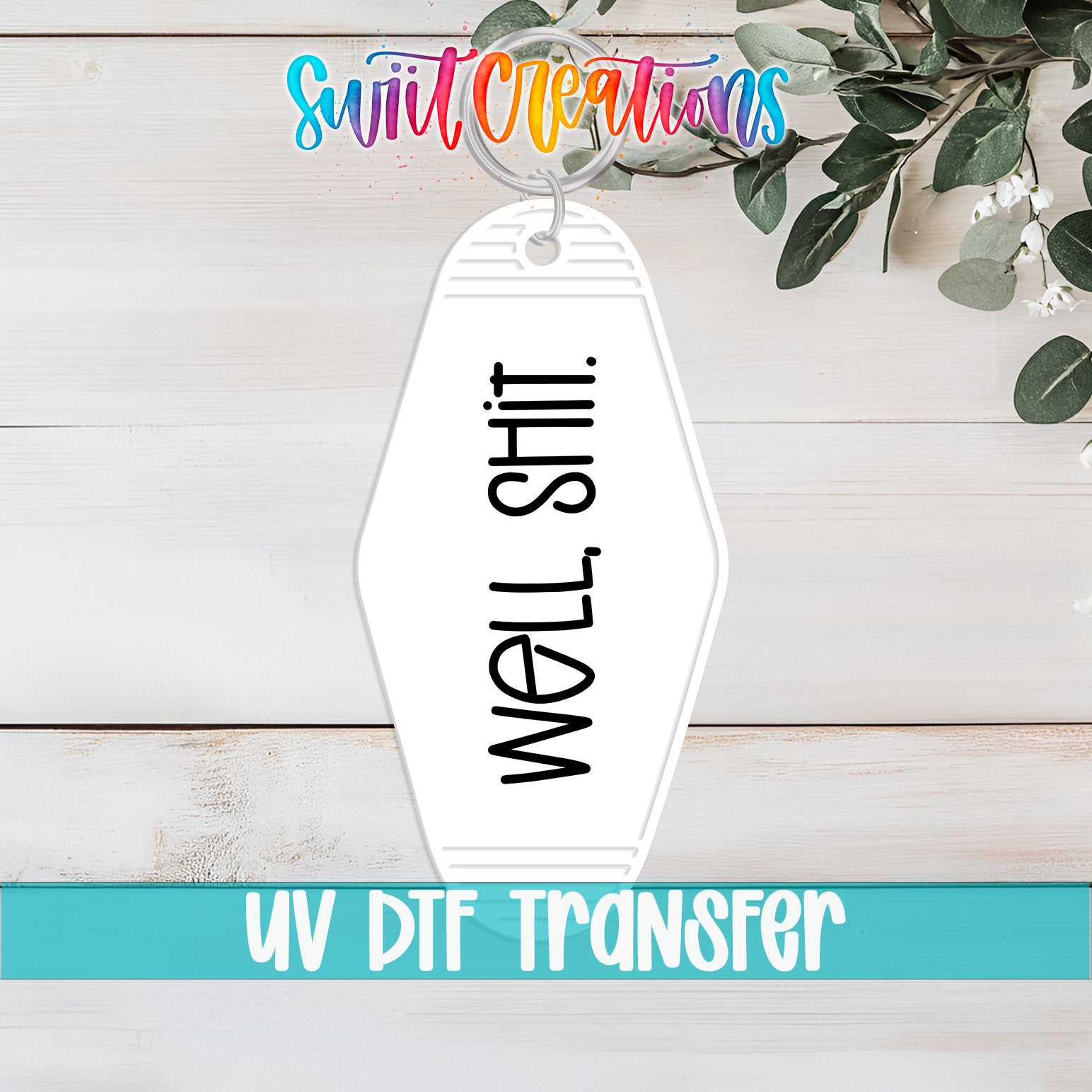A keychain with the text "WELL SHIT" printed on it, placed on a wooden surface with some greenery in the background.