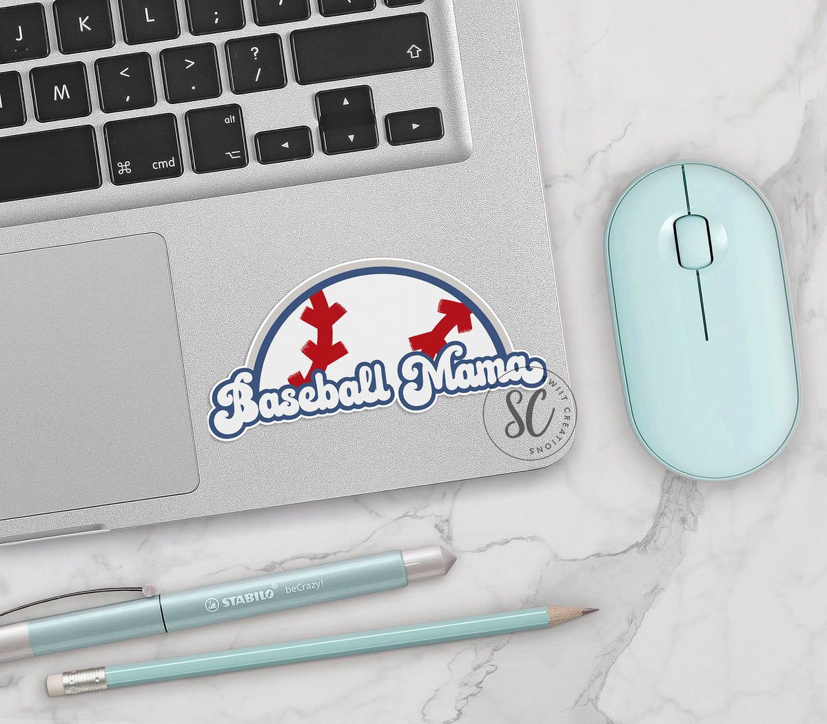 Baseball Mama vinyl sticker on a silver laptop next to a mint mouse and pens
