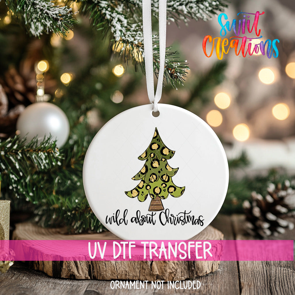 A white Christmas ornament with a leopard print design hangs on a tree, with a blurred background of lights and greenery.