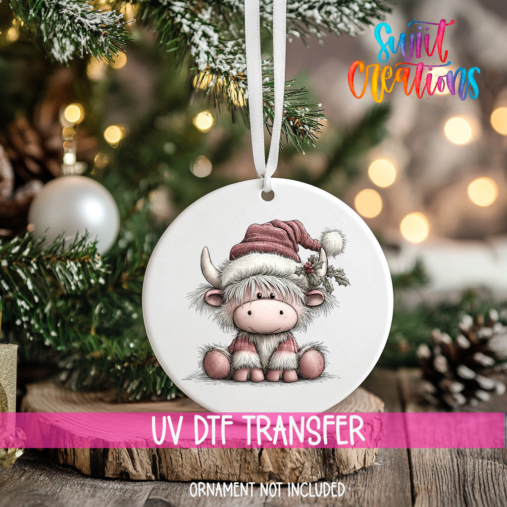 A white ornament with a cartoon cow wearing a Santa hat is hanging on a Christmas tree.