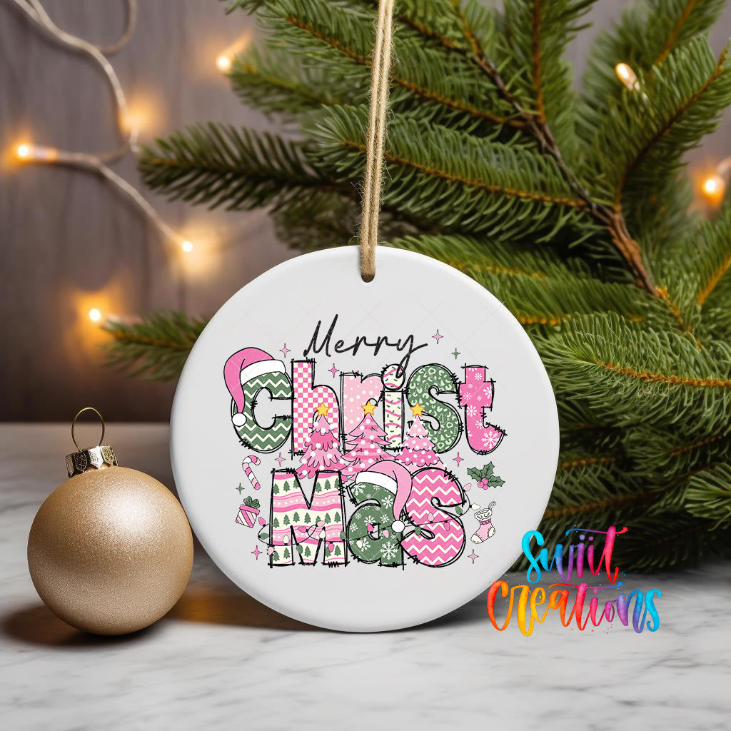 A white ceramic ornament with the text "Merry Christmas" in pink and green colors, hanging on a Christmas tree branch.