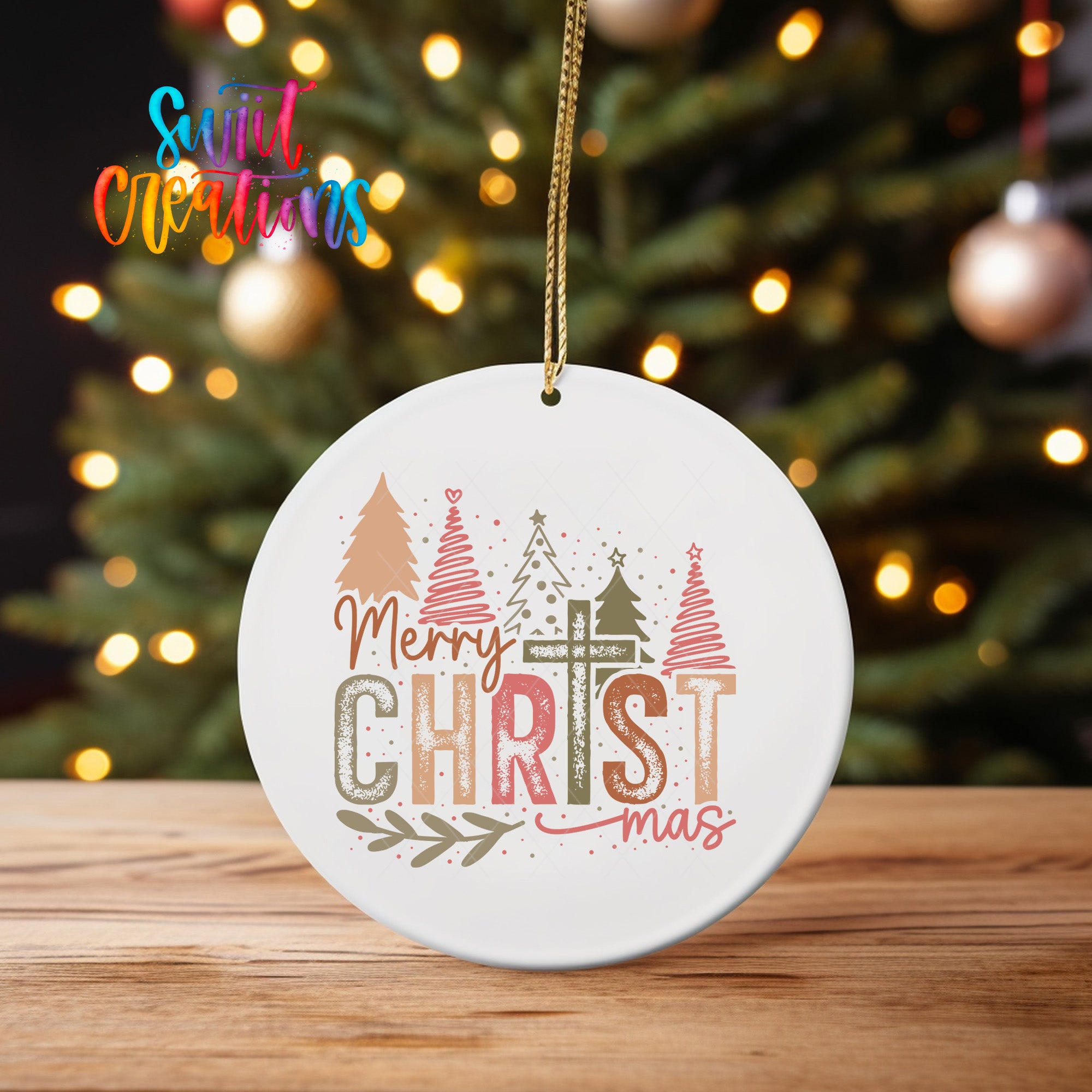 A white Christmas ornament with the text "Merry Christmas" and various Christmas-themed graphics hangs in front of a blurred Christmas tree.