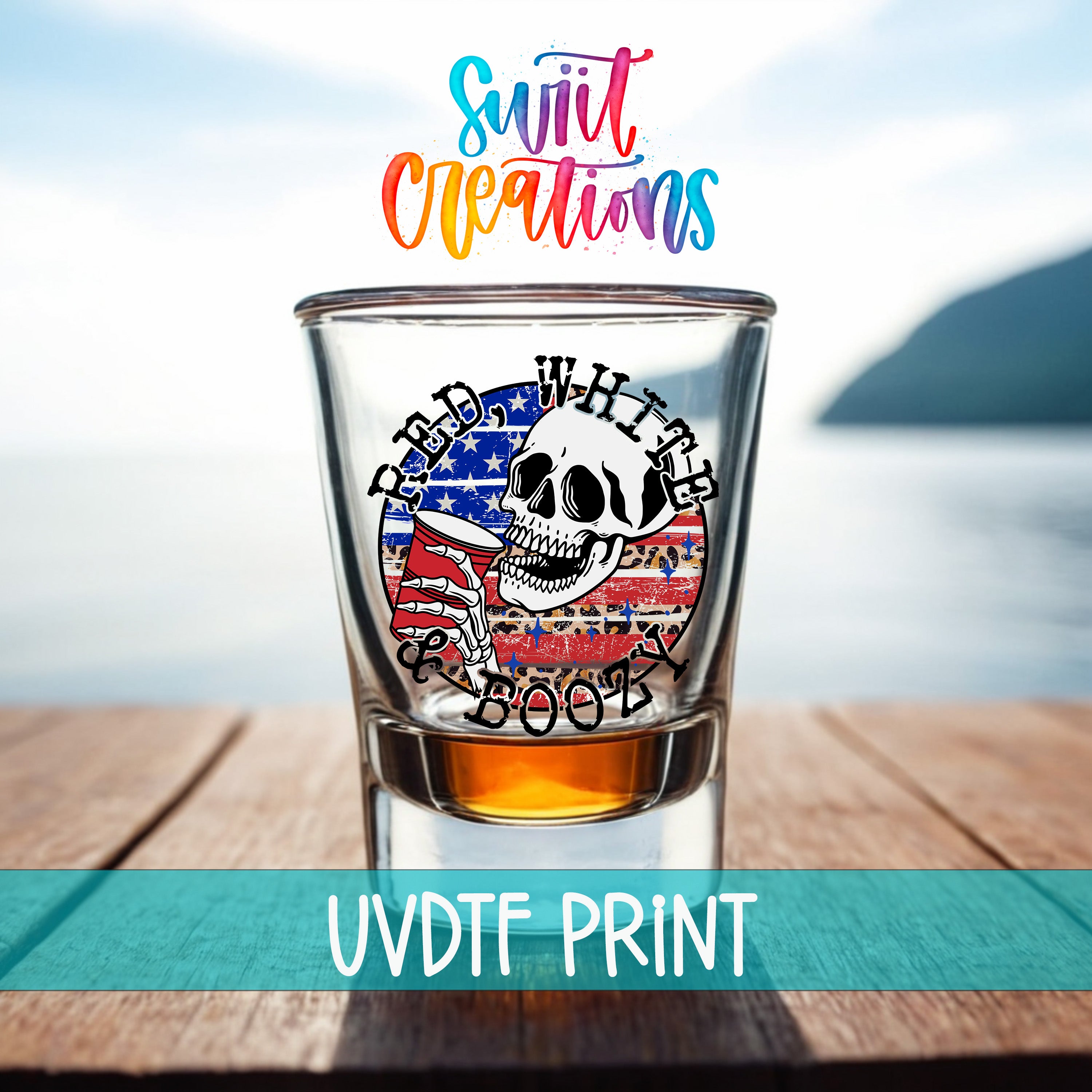 A shot glass with a skull design and an American flag pattern, placed on a wooden surface with a body of water in the background.