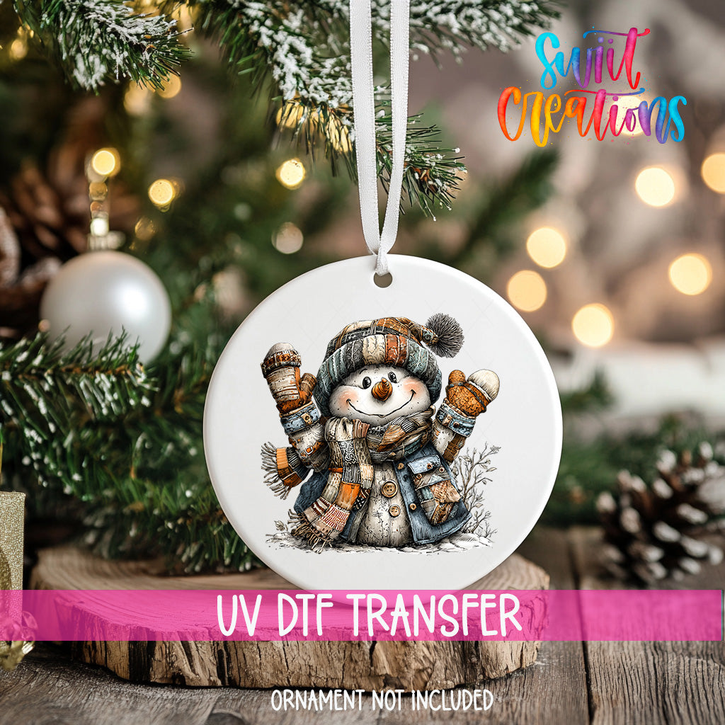 A white ornament with a snowman design hangs on a Christmas tree, surrounded by pine branches and twinkling lights.