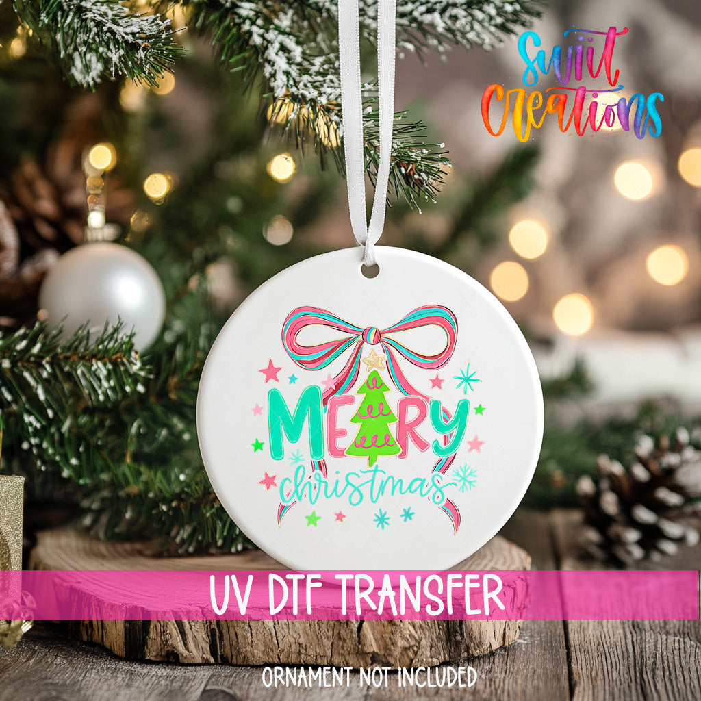 A white Christmas ornament with a colorful design hangs on a tree branch, surrounded by pine needles and other holiday decorations.