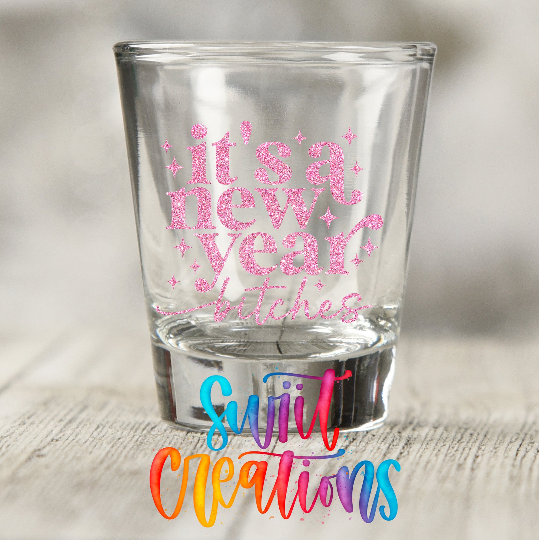 A shot glass with the text "It's a new year, ladies" printed on it, along with a colorful watermark that says "Sult Creations".