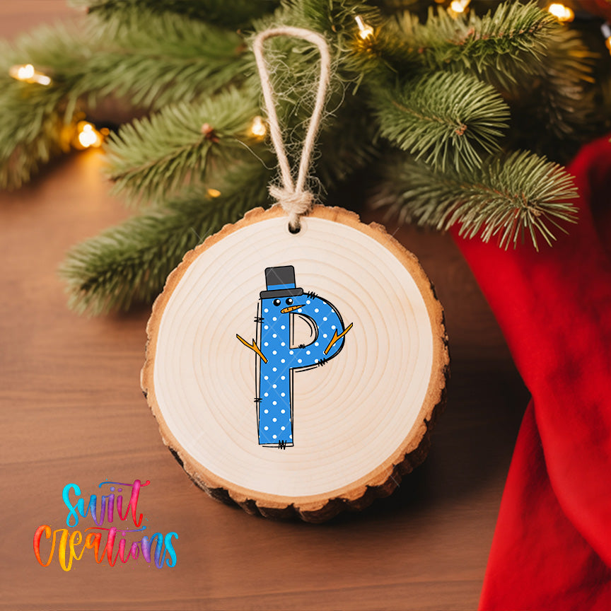 A wooden ornament with a snowman design, featuring the letter "P" in blue with white polka dots, is hanging on a Christmas tree.