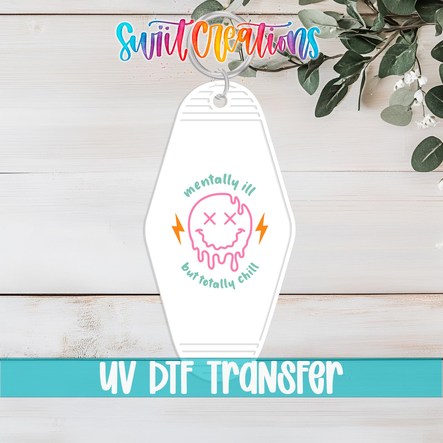 A keychain with a colorful design and text, placed on a wooden surface with greenery in the background.