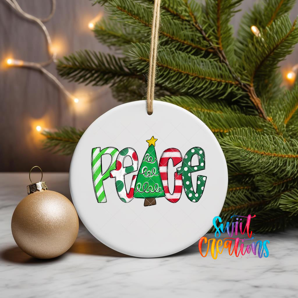 A white ceramic ornament with the word "Peace" written on it, surrounded by Christmas decorations such as a gold ornament and a pine tree.