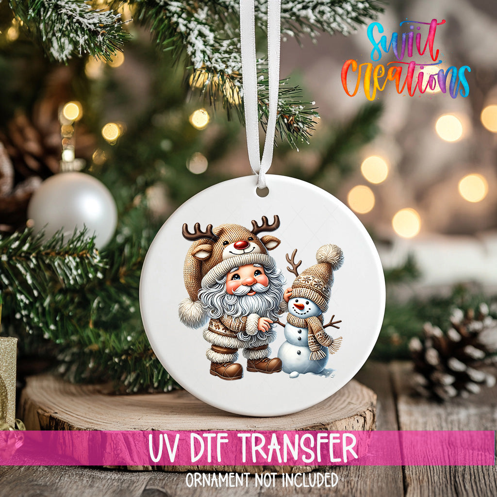 A white ornament with a Santa Claus and a snowman design hangs on a Christmas tree.