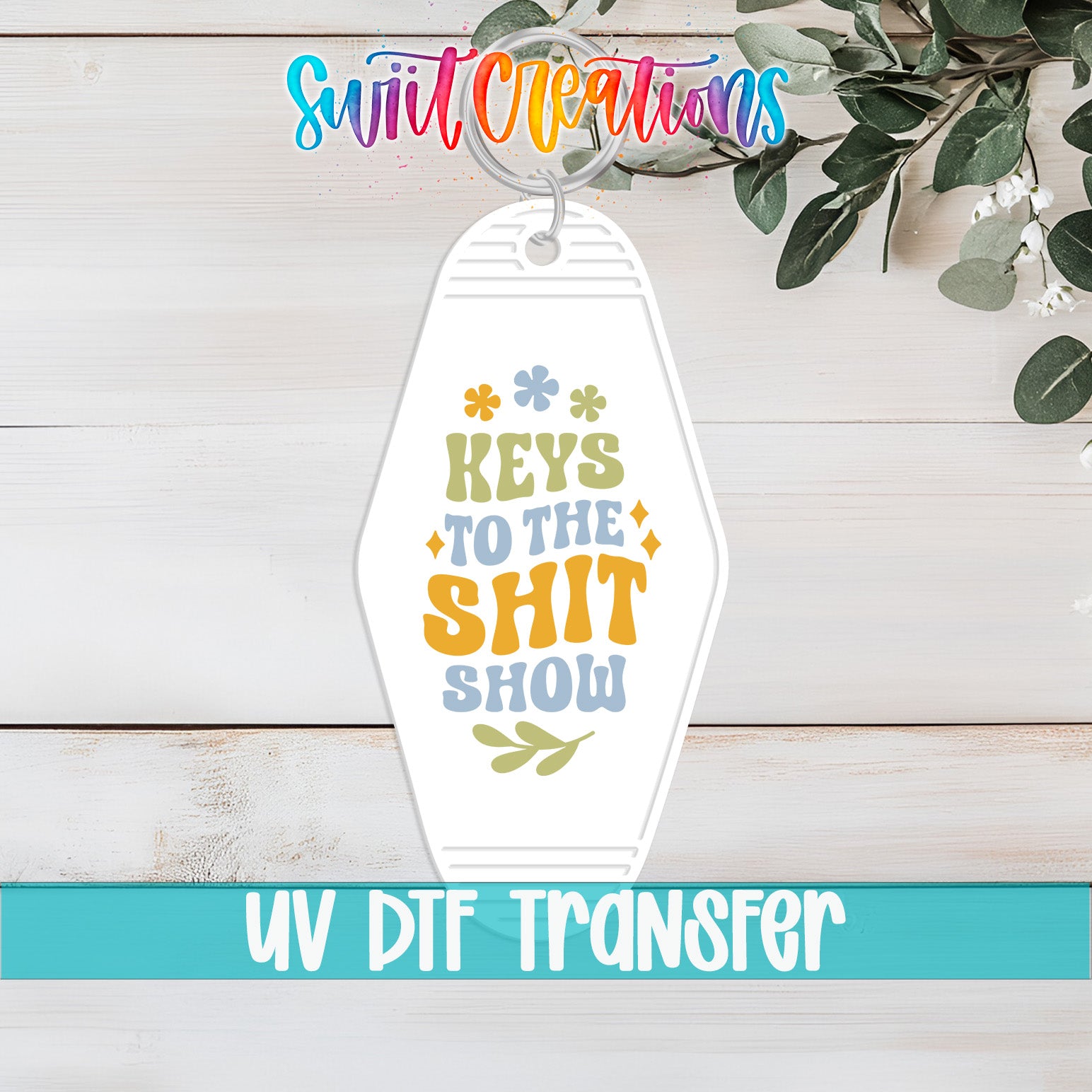 A keychain with the text "Keys to the shit show" printed on it, along with a colorful design featuring flowers and leaves.