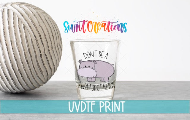 a glass with a hippo on it next to a ball of yarn