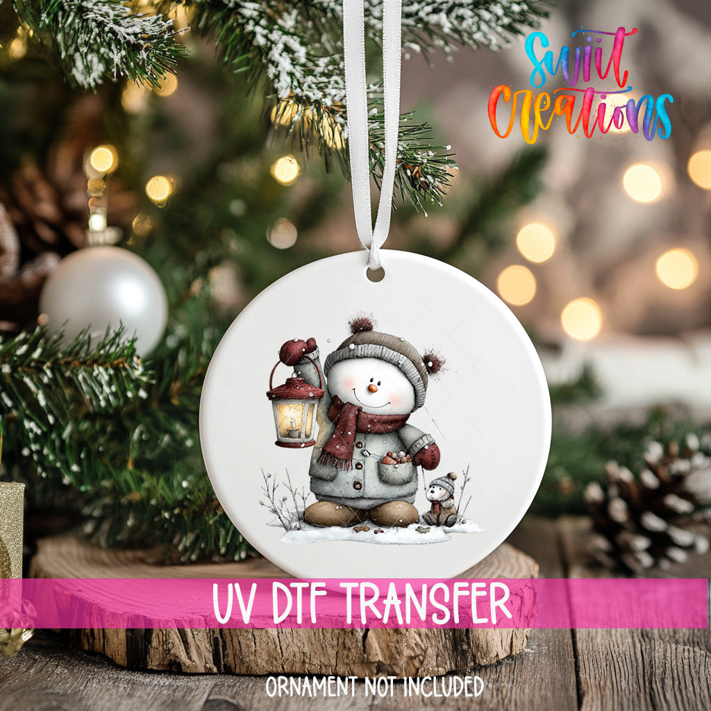 A white ornament with a snowman and lantern hanging on a Christmas tree.