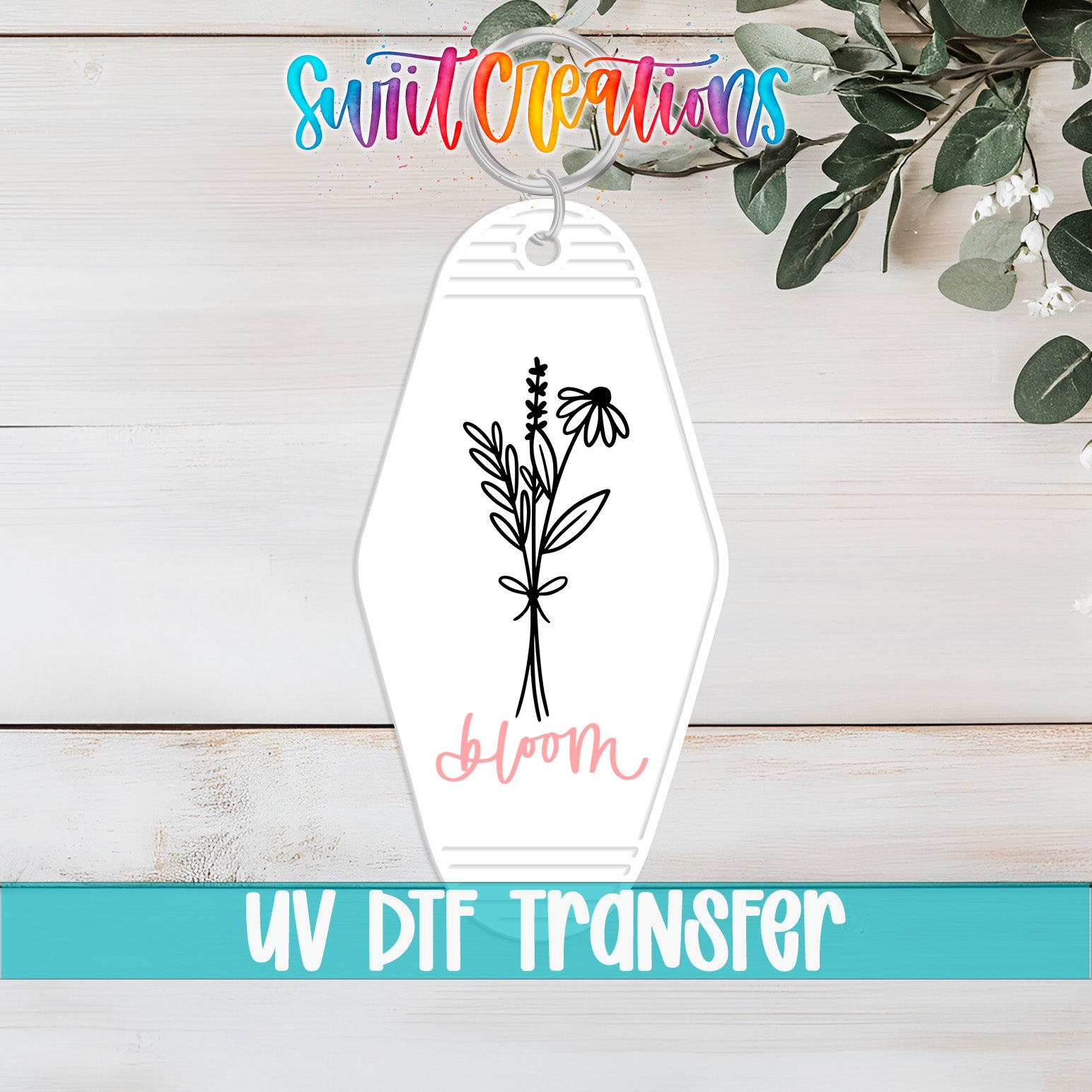 A keychain with a floral design and the word "Bloom" printed on it, placed on a wooden surface with a plant in the background.