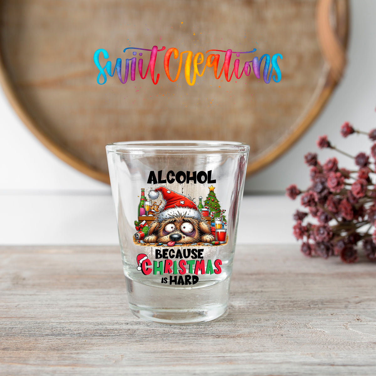 Alcohol Because Christmas is Hard shot glass transfer on a clear glass beside a wooden barrel and dried flowers