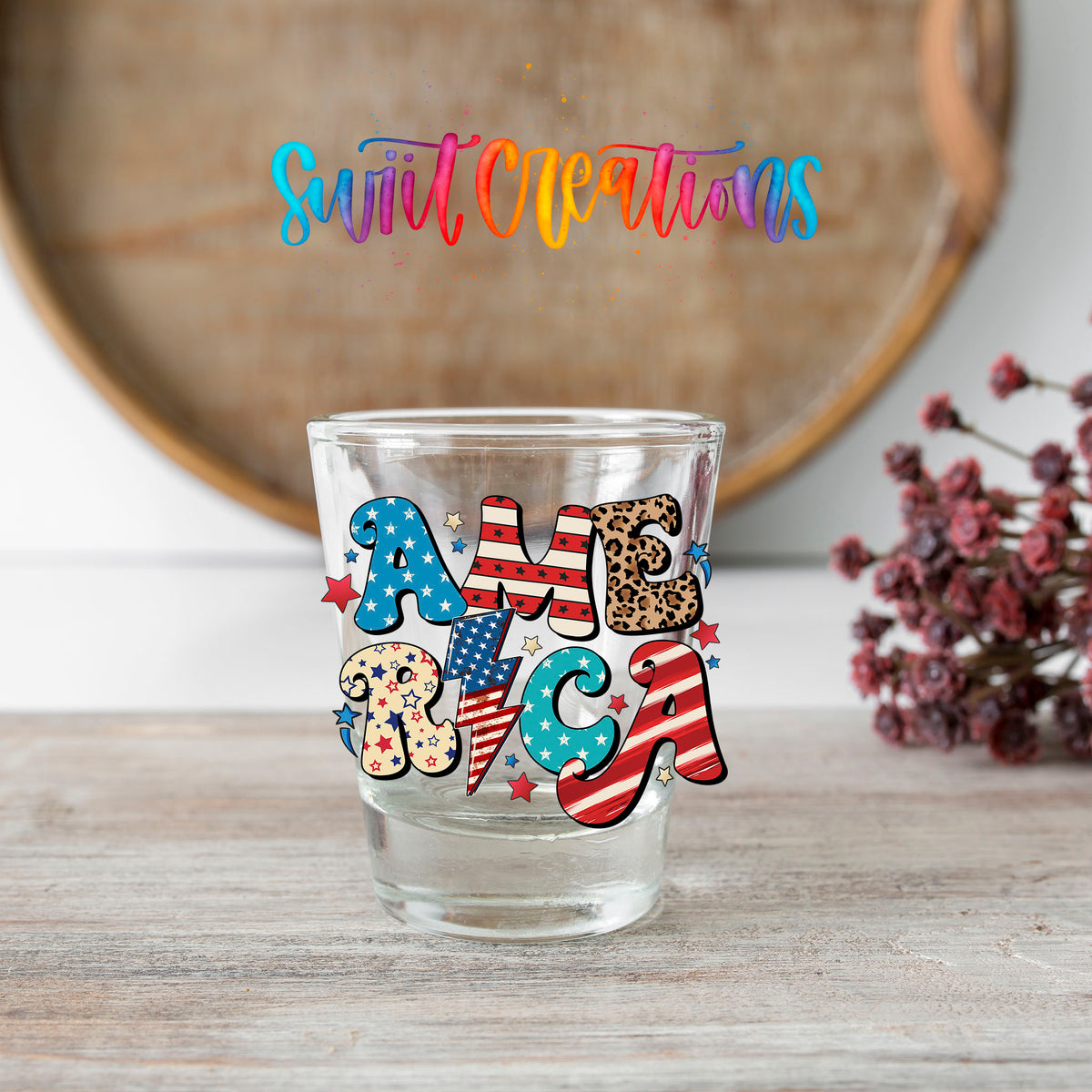 America shot glass transfer on a clear glass beside a wooden barrel and dried flowers