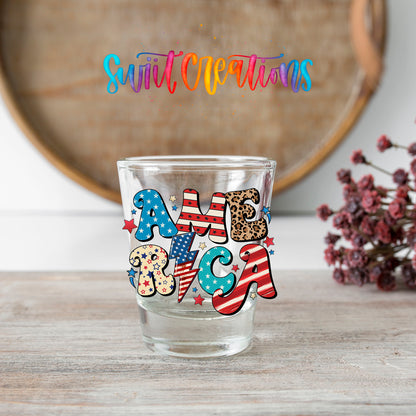 America shot glass transfer on a clear glass beside a wooden barrel and dried flowers