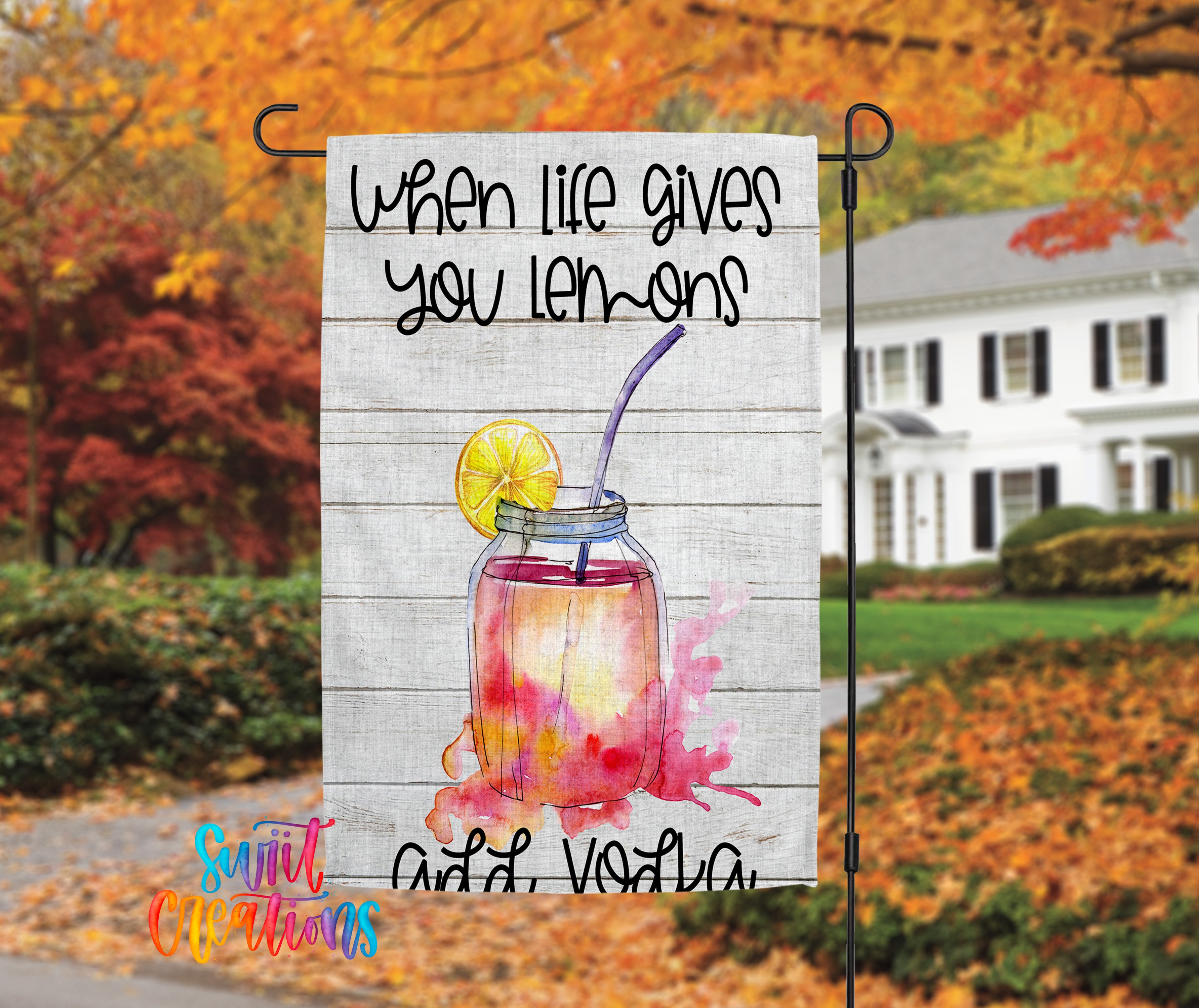 A banner with a lemonade drink and a lemon slice, hanging in front of a house with autumn foliage in the background.