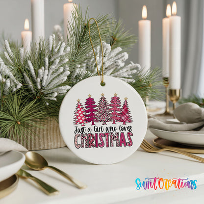 A white ceramic ornament with a Christmas tree design and text that says "Just a Girl Who Loves Christmas" is displayed on a table with candles and other holiday decorations.
