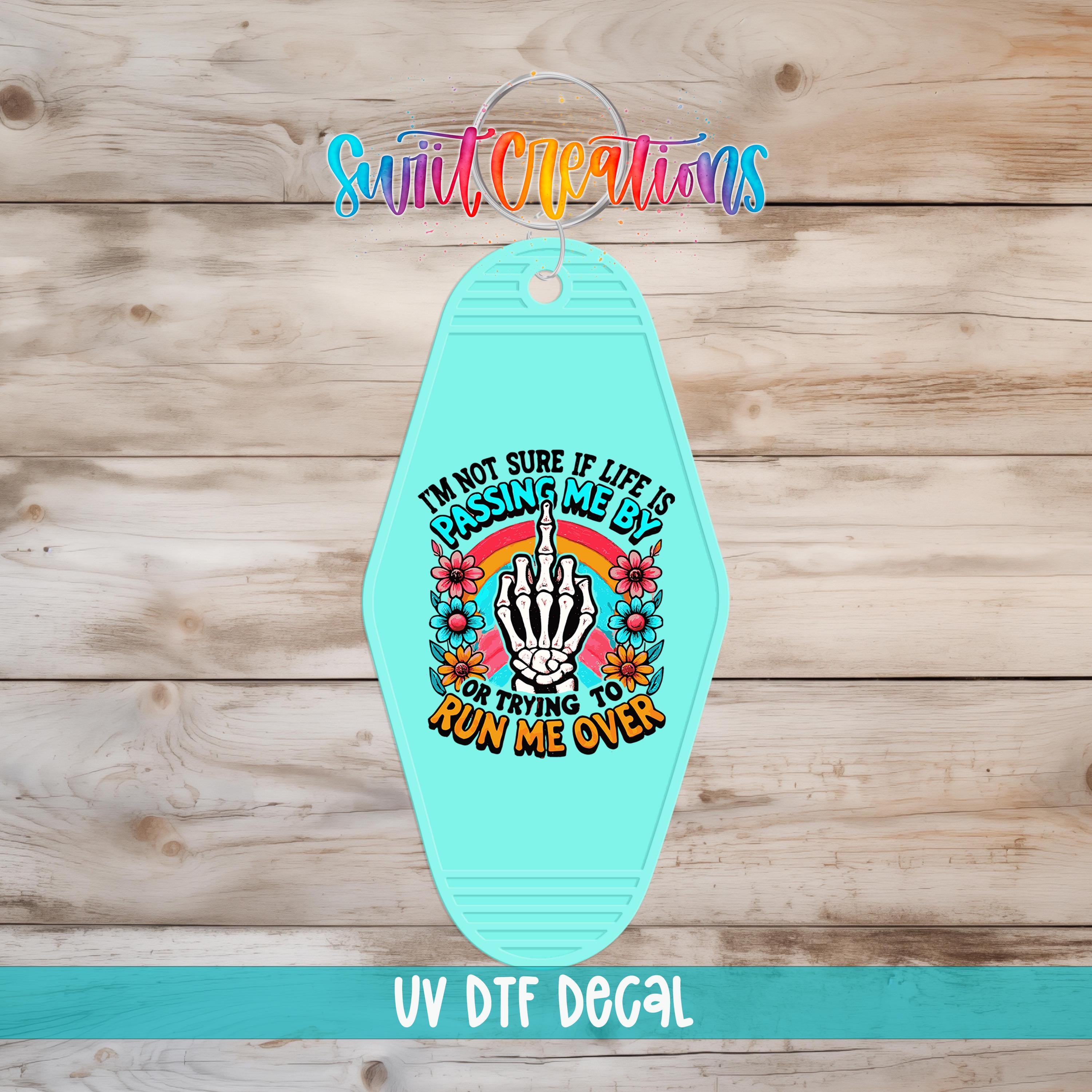 A turquoise keychain with a colorful graphic design and text on it, placed on a wooden surface.