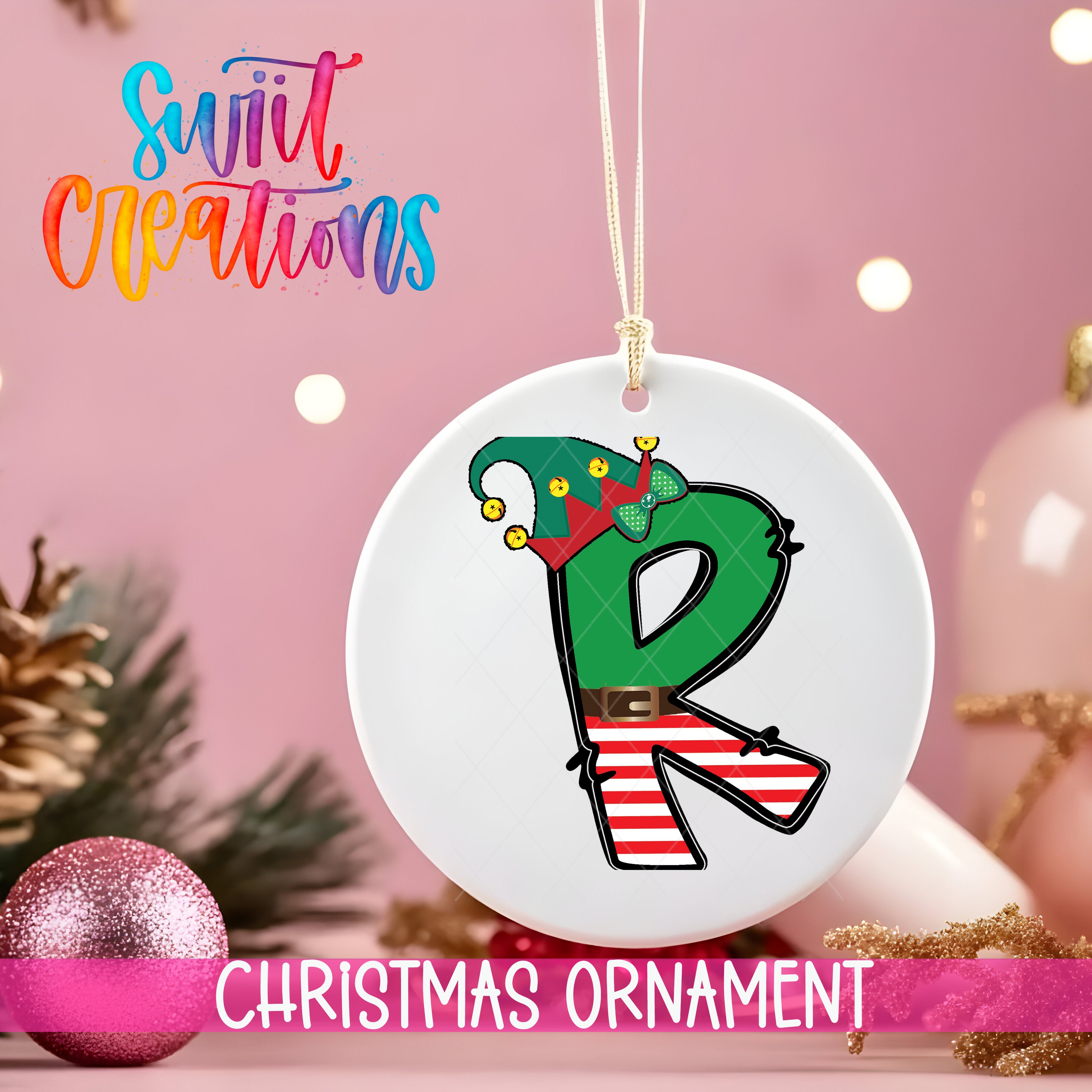 A white Christmas ornament with a green elf hat and red bow, hanging on a string against a pink background.