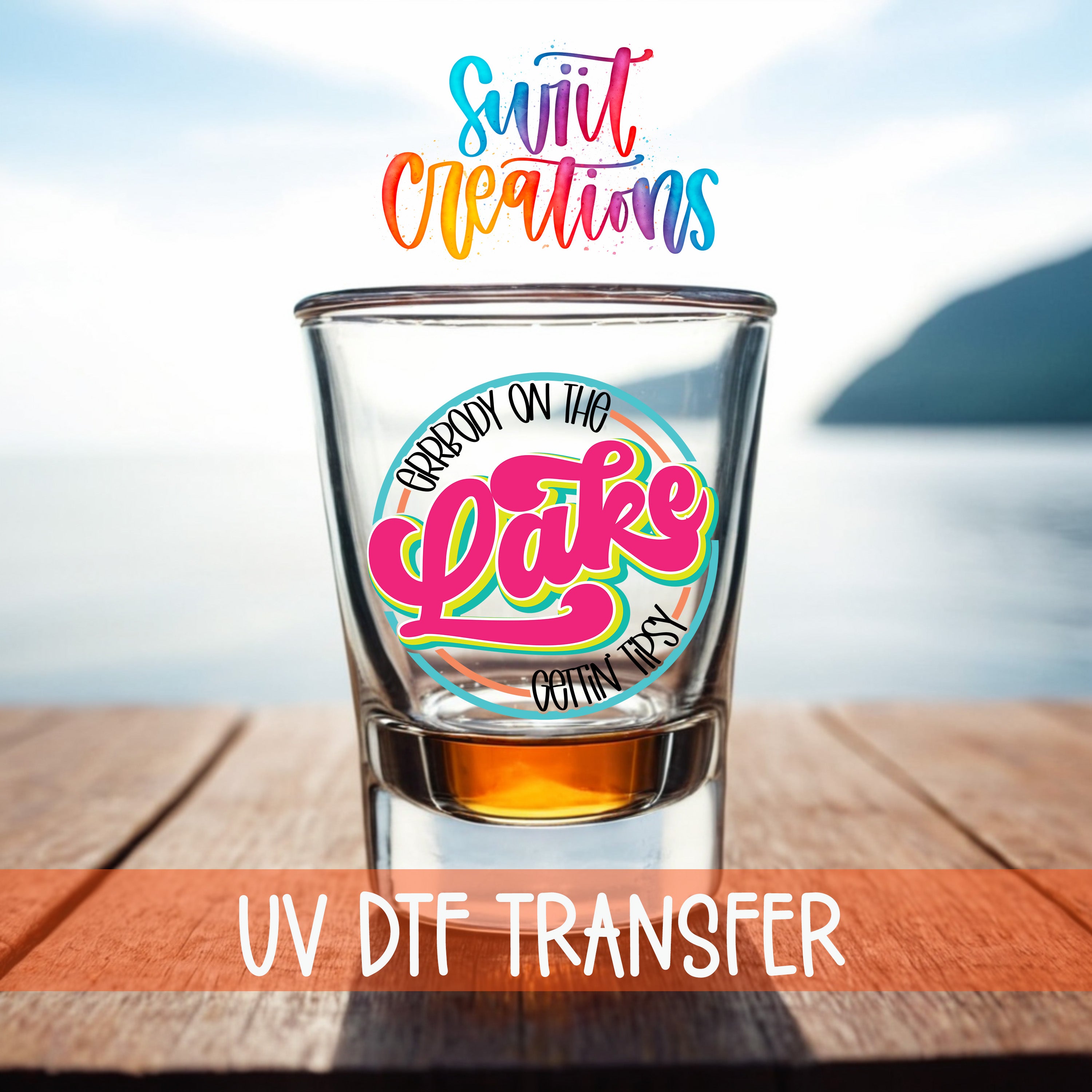 a shot glass with a colorful design on it, placed on a wooden surface with a body of water in the background.