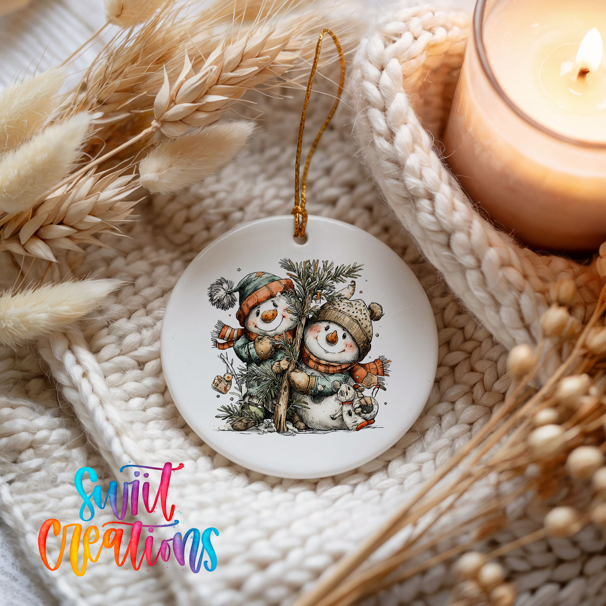 A ceramic ornament featuring two snowmen, one wearing a green hat and the other a red hat, is displayed on a knitted blanket. A lit candle is also present in the scene.