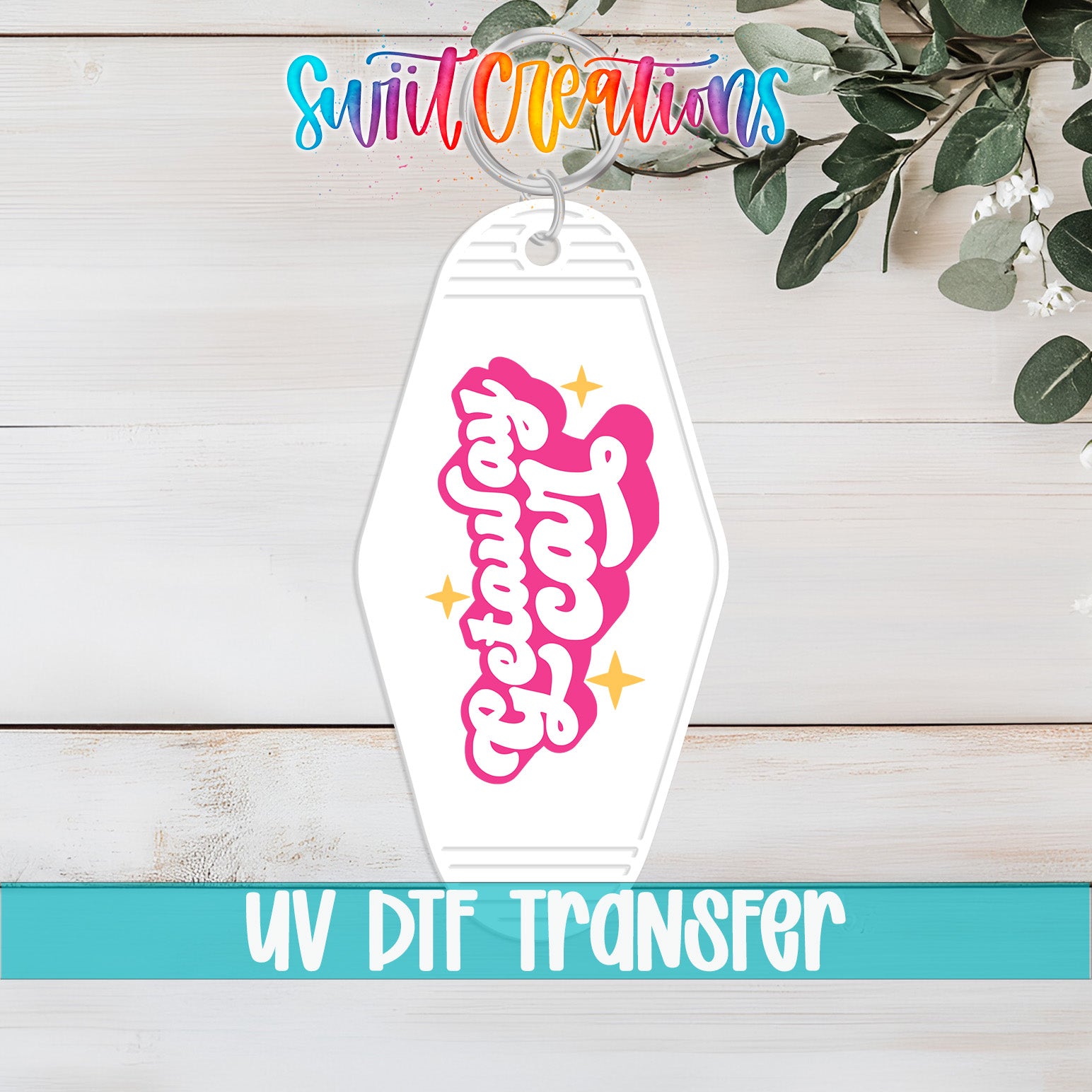 A keychain with a colorful design and text, placed on a wooden surface with greenery in the background.