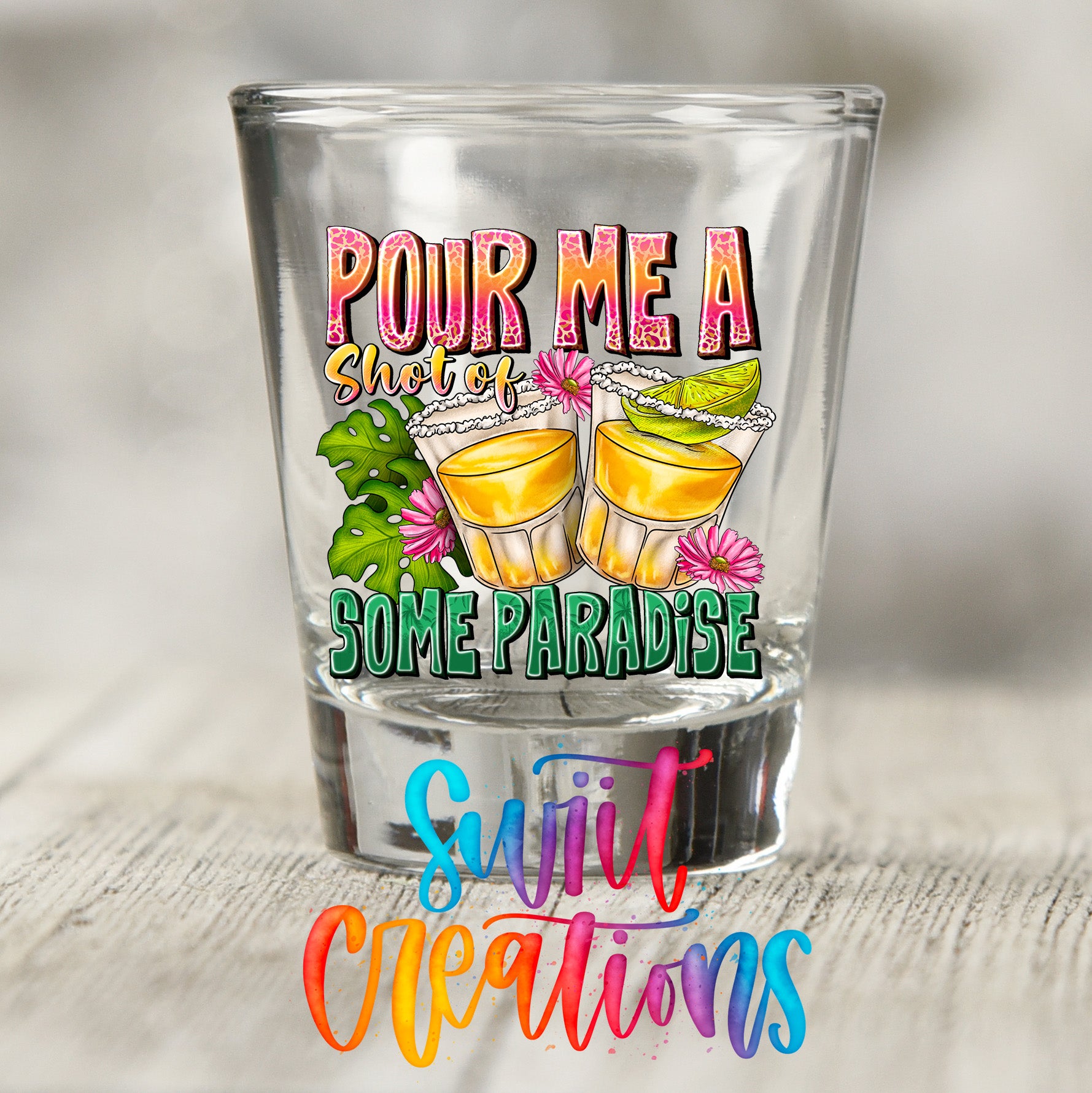 a shot glass with a colorful design and text that reads "POUR ME A SHOT OF SOME PARADISE" and "SWEET CREATIONS".