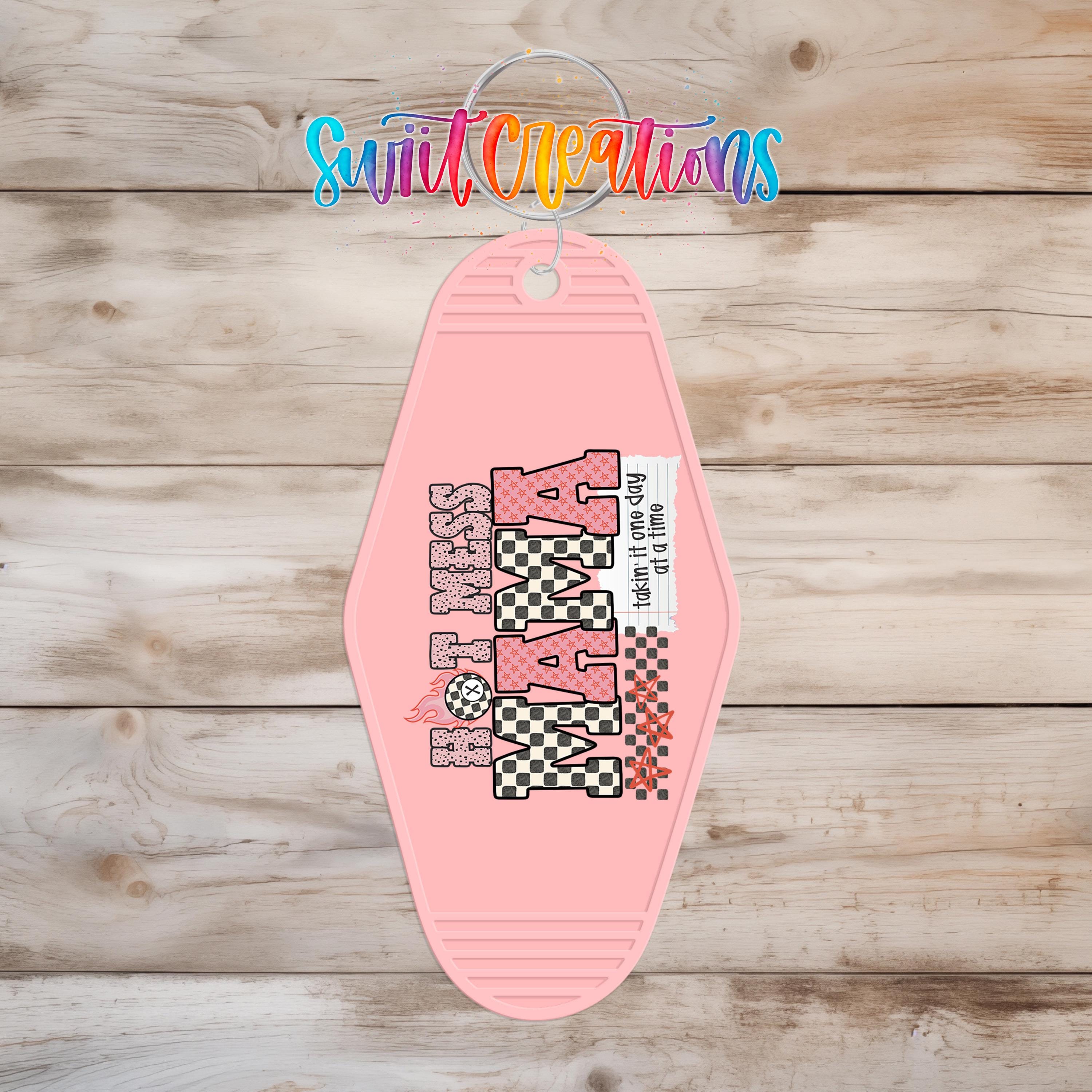 A pink keychain with the text "HOT MOM" printed on it, hanging on a wooden surface.