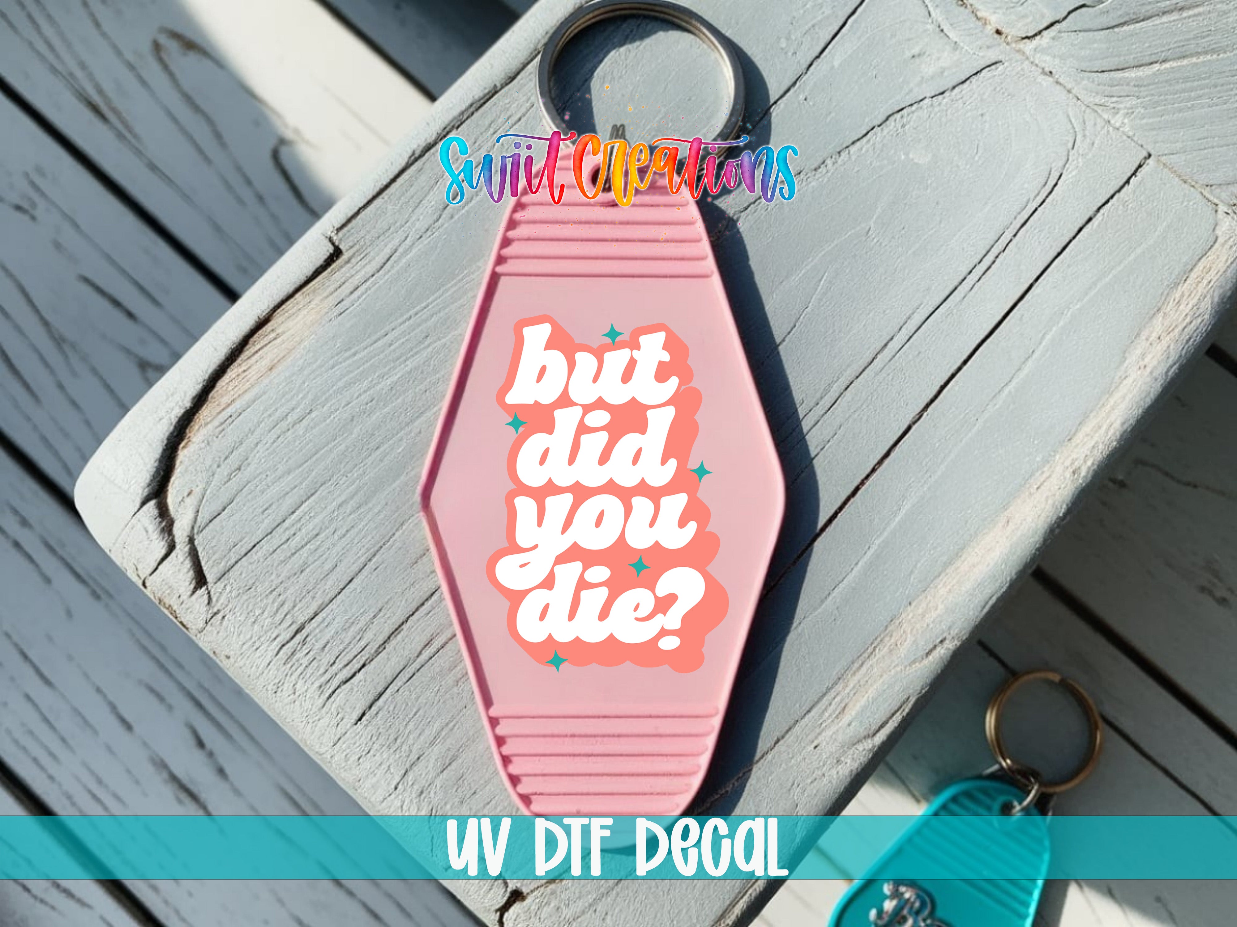 A pink keychain with the text "but did you die?" printed on it, placed on a wooden surface.