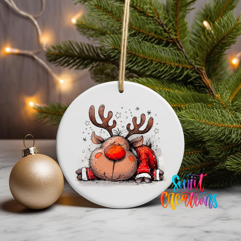 A white ornament with a cartoon reindeer design is displayed on a table, surrounded by a Christmas tree and twinkling lights.
