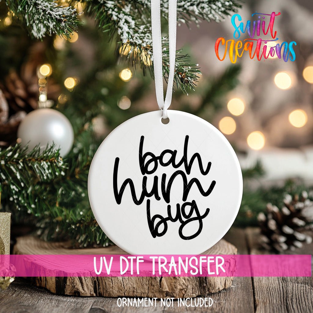 Bah Humbug ornament UV DTF transfer on an ornament resting on a wood slice beside a Christmas tree