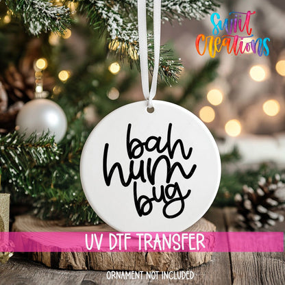 Bah Humbug ornament UV DTF transfer on an ornament resting on a wood slice beside a Christmas tree