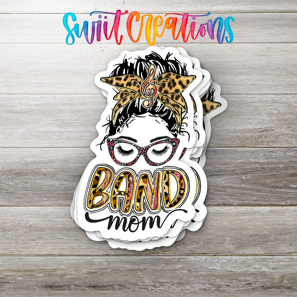Stack of Leopard Messy Bun Band Mom glossy stickers on a gray wood table