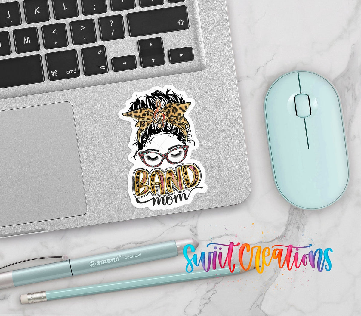 Leopard Messy Bun Band Mom vinyl sticker on a silver laptop next to a mint mouse and pens