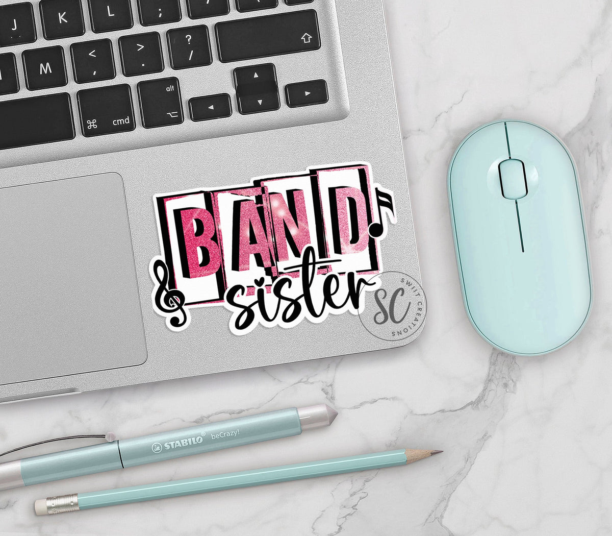 Pink Band Sister vinyl sticker on a silver laptop next to a mint mouse and pens