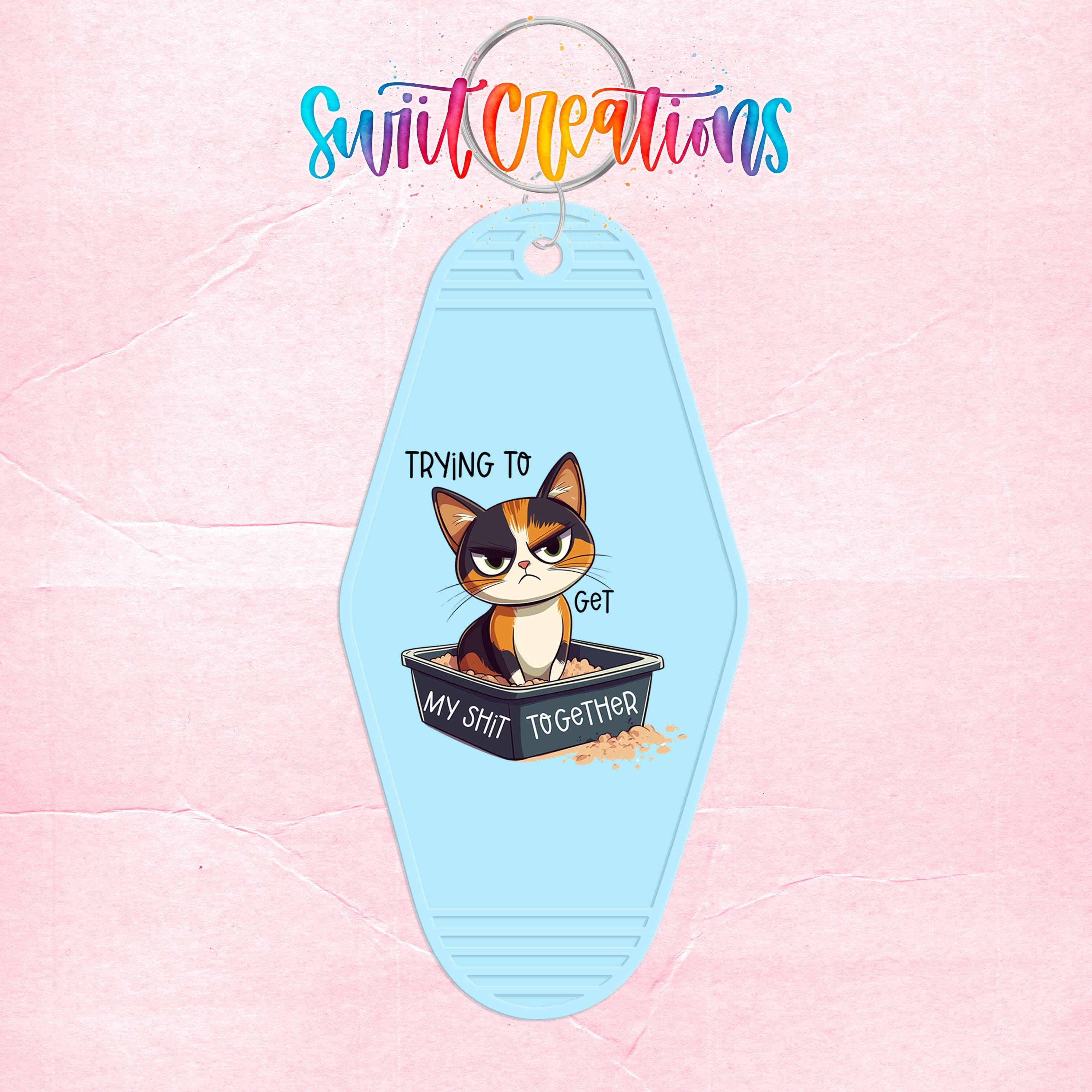 A keychain with a cartoon cat and the text "Trying to get my shit together" printed on it.