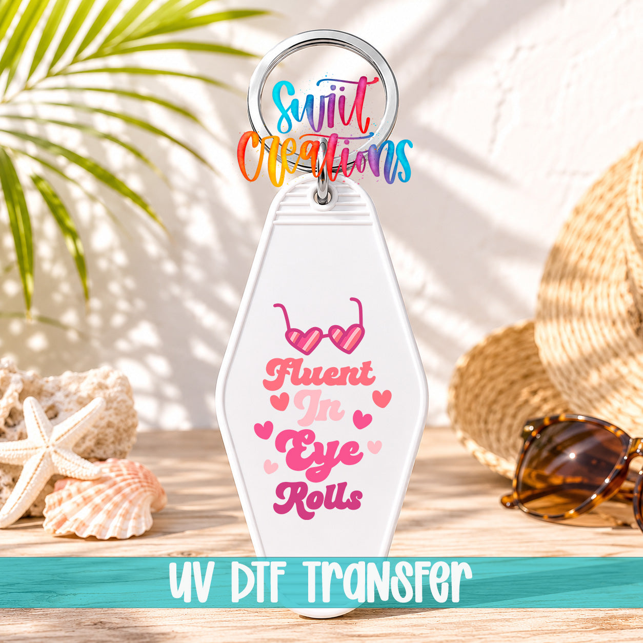 A keychain with a message that says "Fluent in Eye Rolls" and sunglasses on it, placed on a wooden surface with a straw hat and seashells in the background.