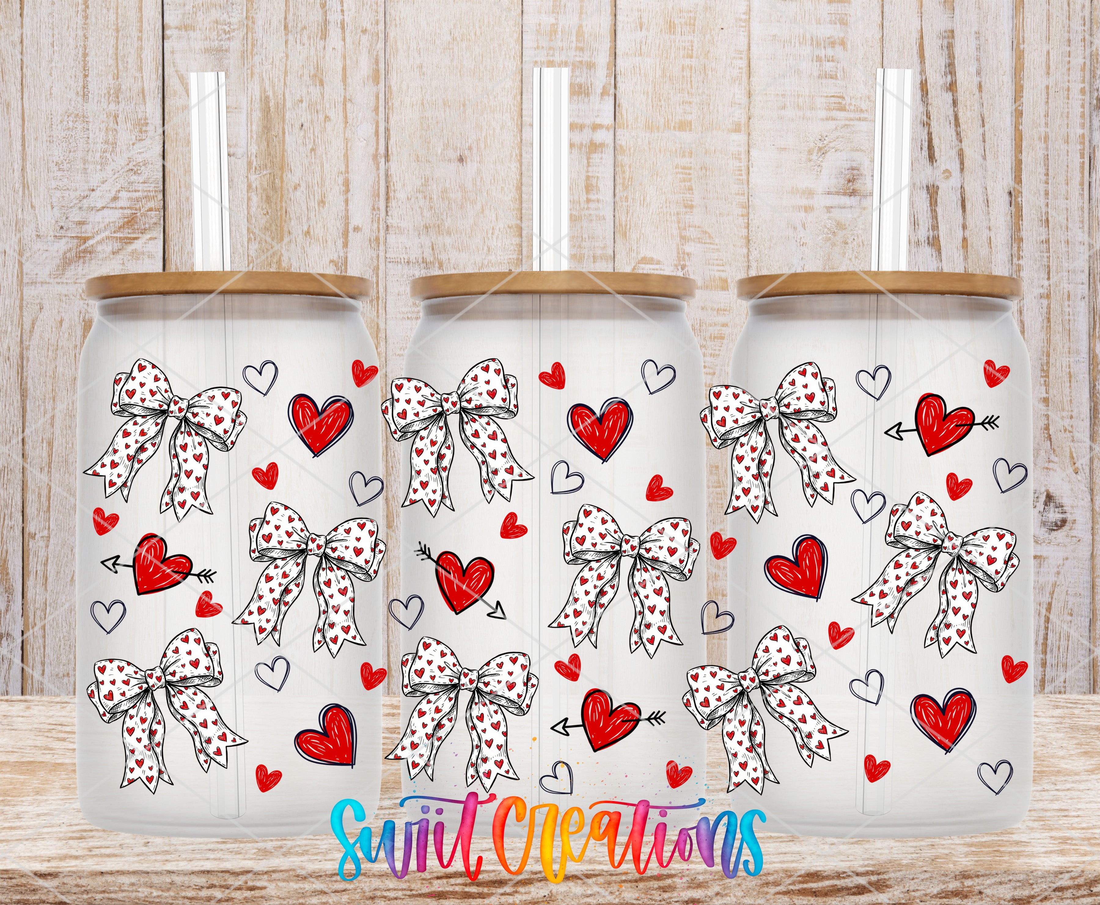 Three white glass tumblers with bow designs and heart and heart motifs are arranged in a row on a wooden surface.