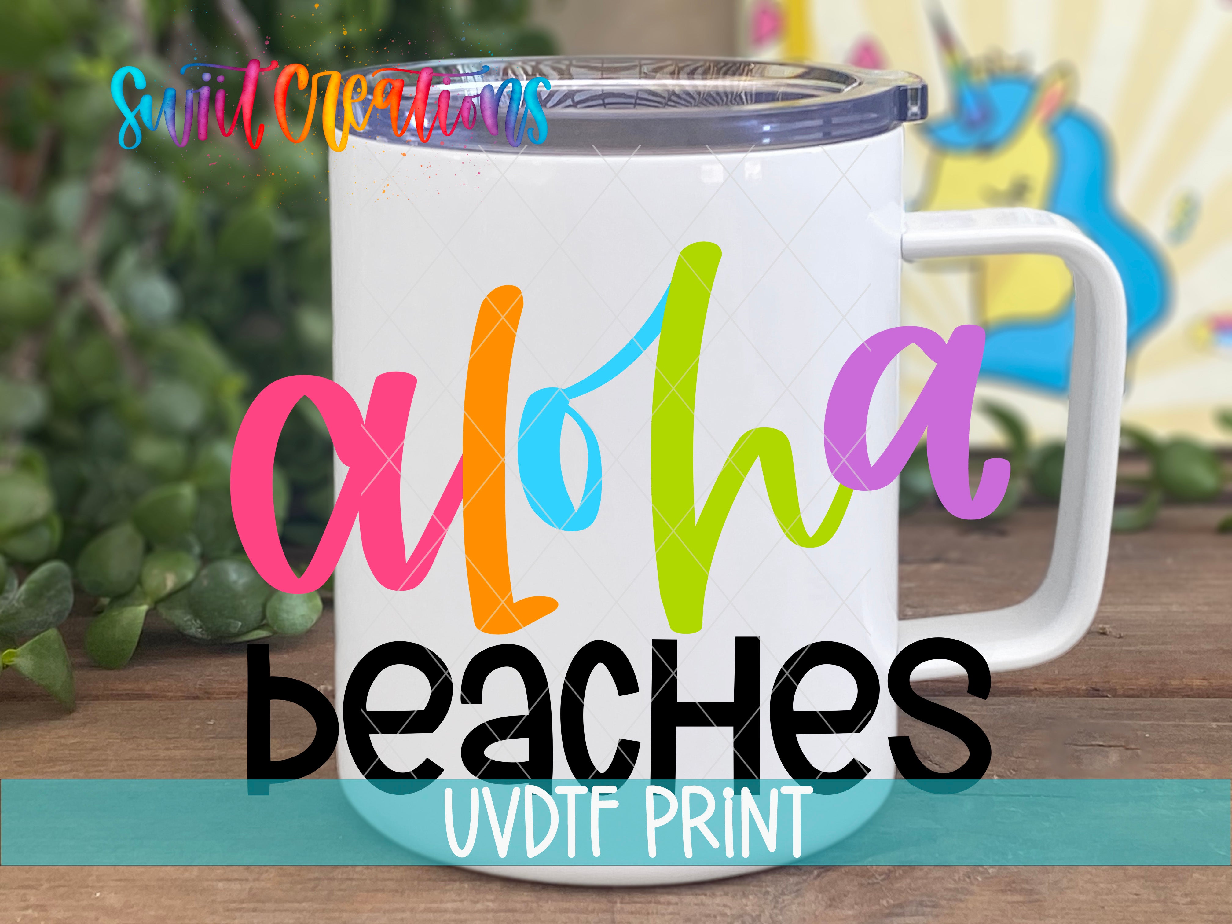A colorful mug with the text "Aloha Beaches UVDF PRINT" printed on it, placed on a wooden surface with a blurred background.