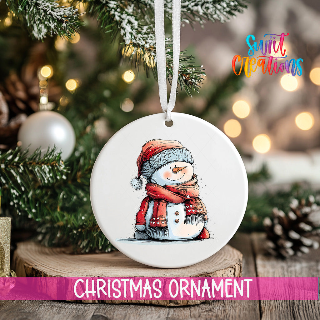 A white Christmas ornament featuring a snowman is hanging from a ribbon, with a blurred background of a decorated Christmas tree and other ornaments.