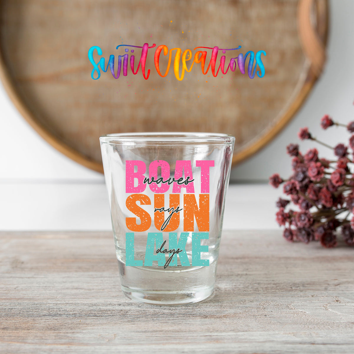 Boat Waves Sun Rays Lake Days shot glass transfer on a clear glass beside a wooden barrel and dried flowers