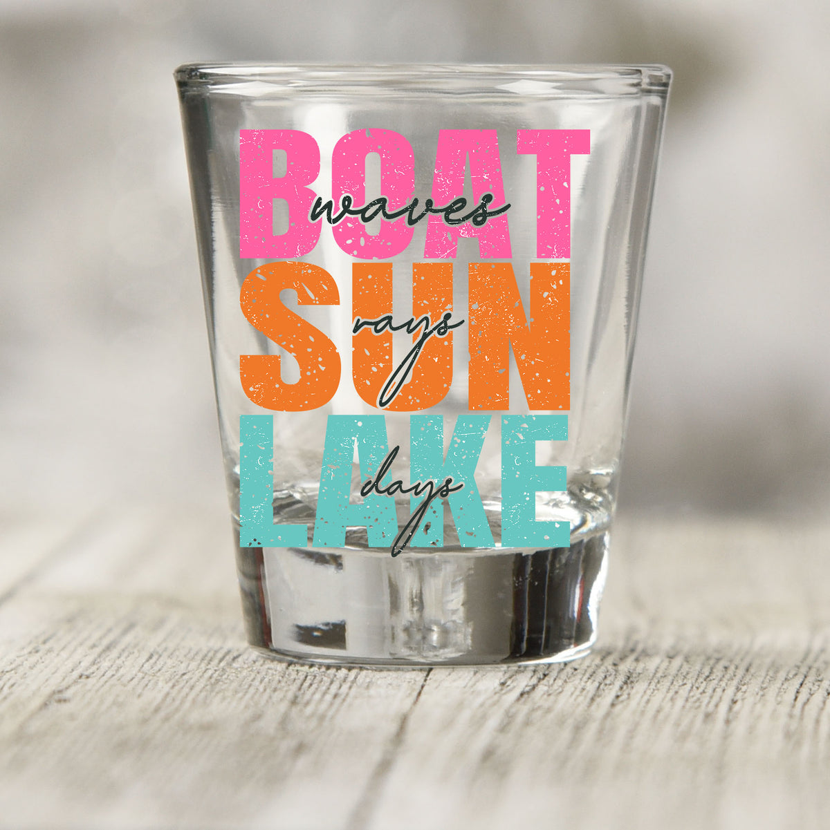 Boat Waves Sun Rays Lake Days shot glass UV DTF transfer with stacked block and script lettering on a clear shot glass