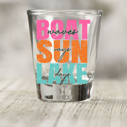 Boat Waves Sun Rays Lake Days shot glass UV DTF transfer with stacked block and script lettering on a clear shot glass