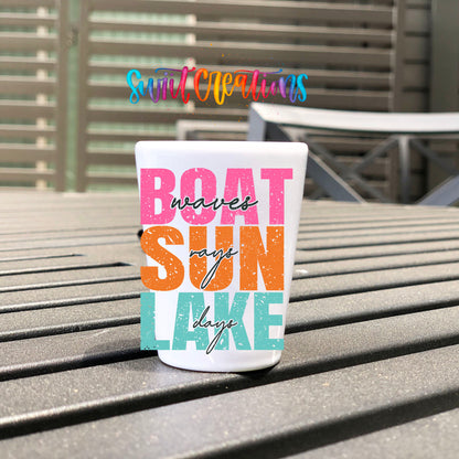 Boat Waves Sun Rays Lake Days UV DTF transfer on a white shot glass on an outdoor patio table