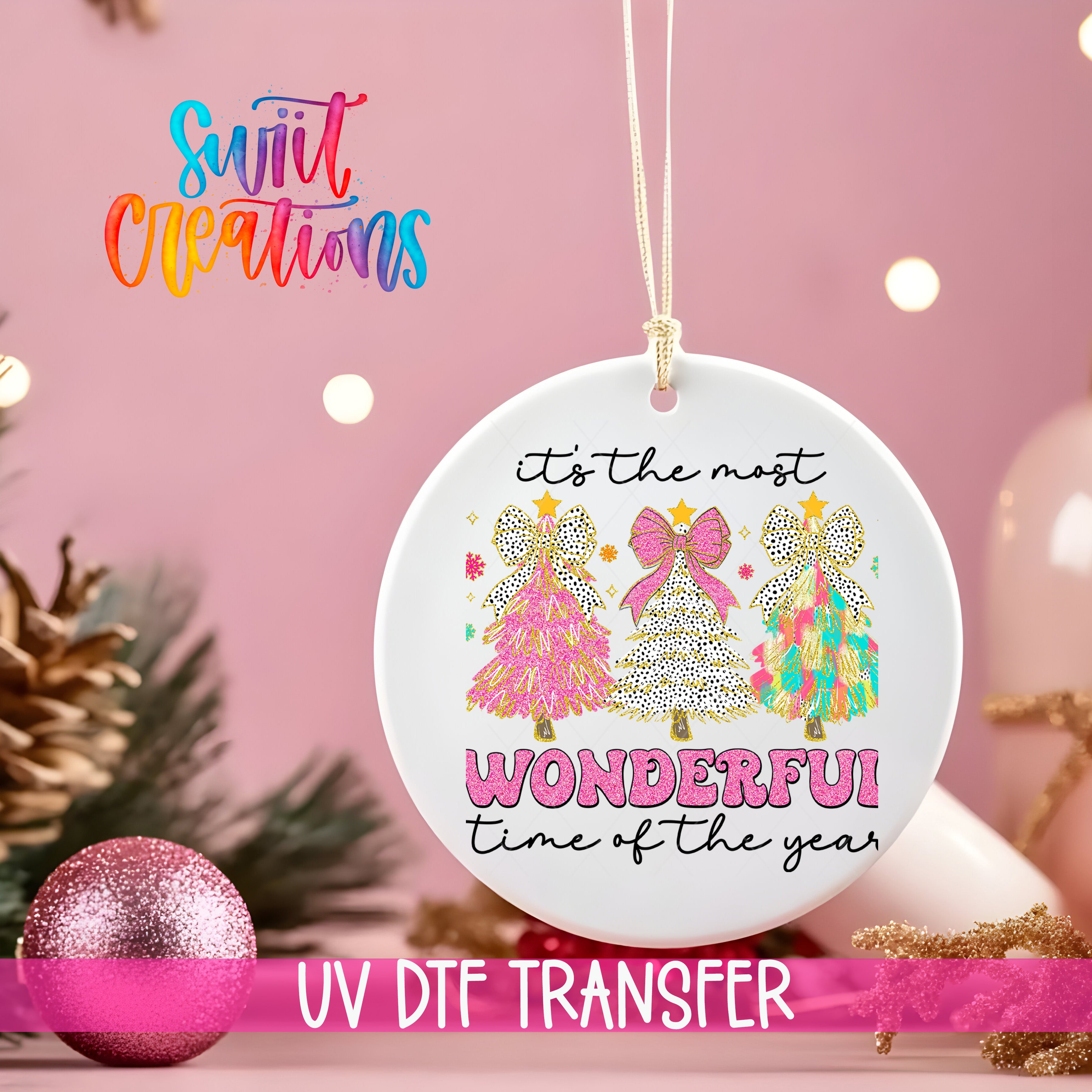 A white ornament with a festive design hangs against a pink background, accompanied by a pink glitter ball and a pink ribbon.