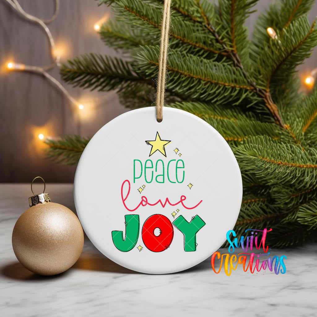 A white ceramic ornament with the text "Peace love joy" is displayed on a table, surrounded by a Christmas tree and twinkling lights.
